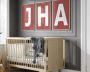 Three framed Nantucket red and white letter art prints spelling out a baby's initials or monogram hanging above a crib in a neutral nursery.