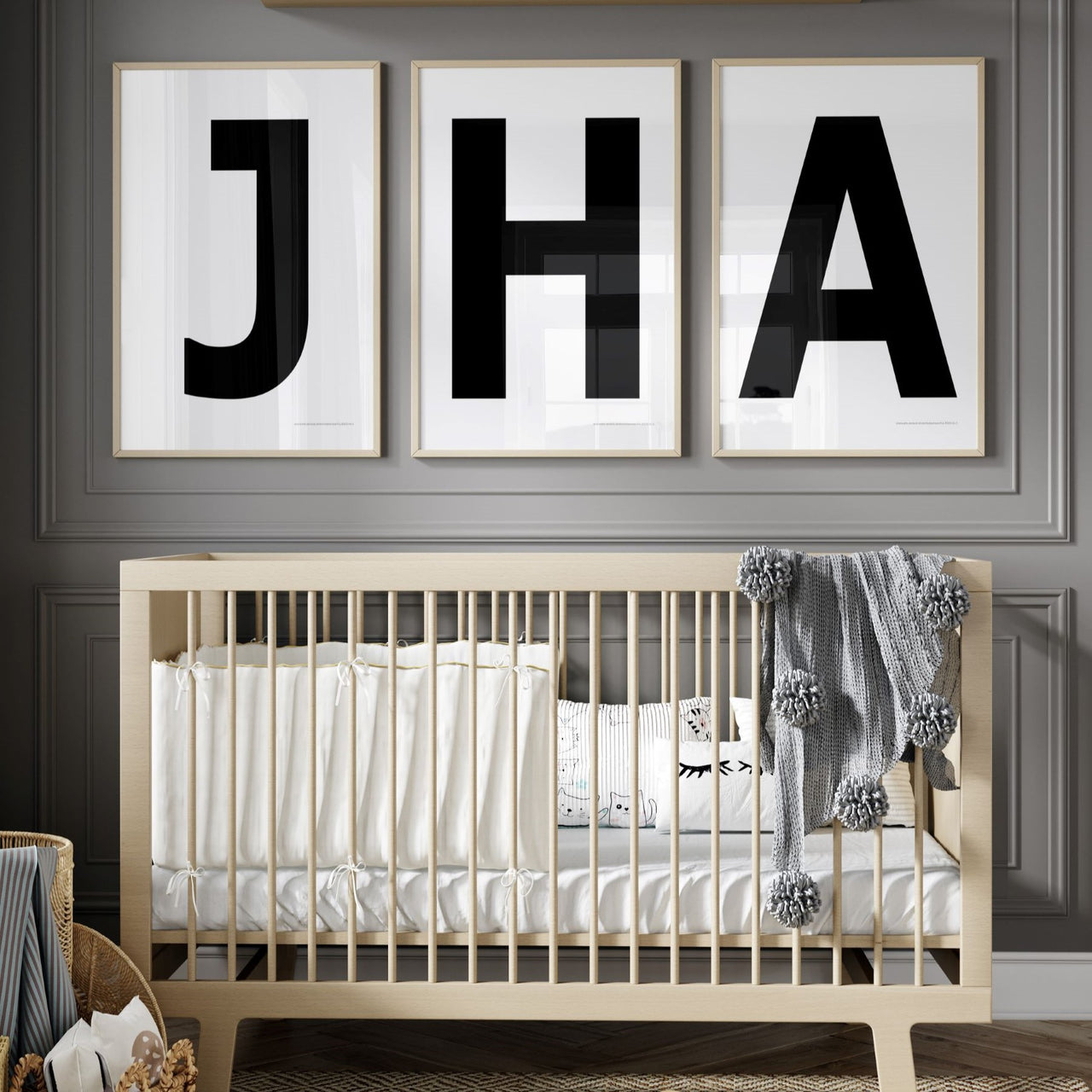 Three framed white and black letter art prints spelling out a baby's initials or monogram above a crib in a gray nursery.