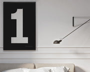 Framed white and black number 1 art print hanging on a wall above a bed in a modern bedroom.