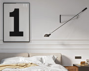 Framed white and black number 1 art print hanging on a wall above a bed in a modern bedroom.