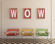 Three framed letter art prints that spell WOW hanging on wall above three modern colorful chairs.