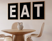 Three framed black and white letter art prints spelling out the word EAT hanging in a modern dining room.