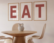 Three framed Nantucket red and white letter art prints spelling out the word EAT hanging in a modern dining room.