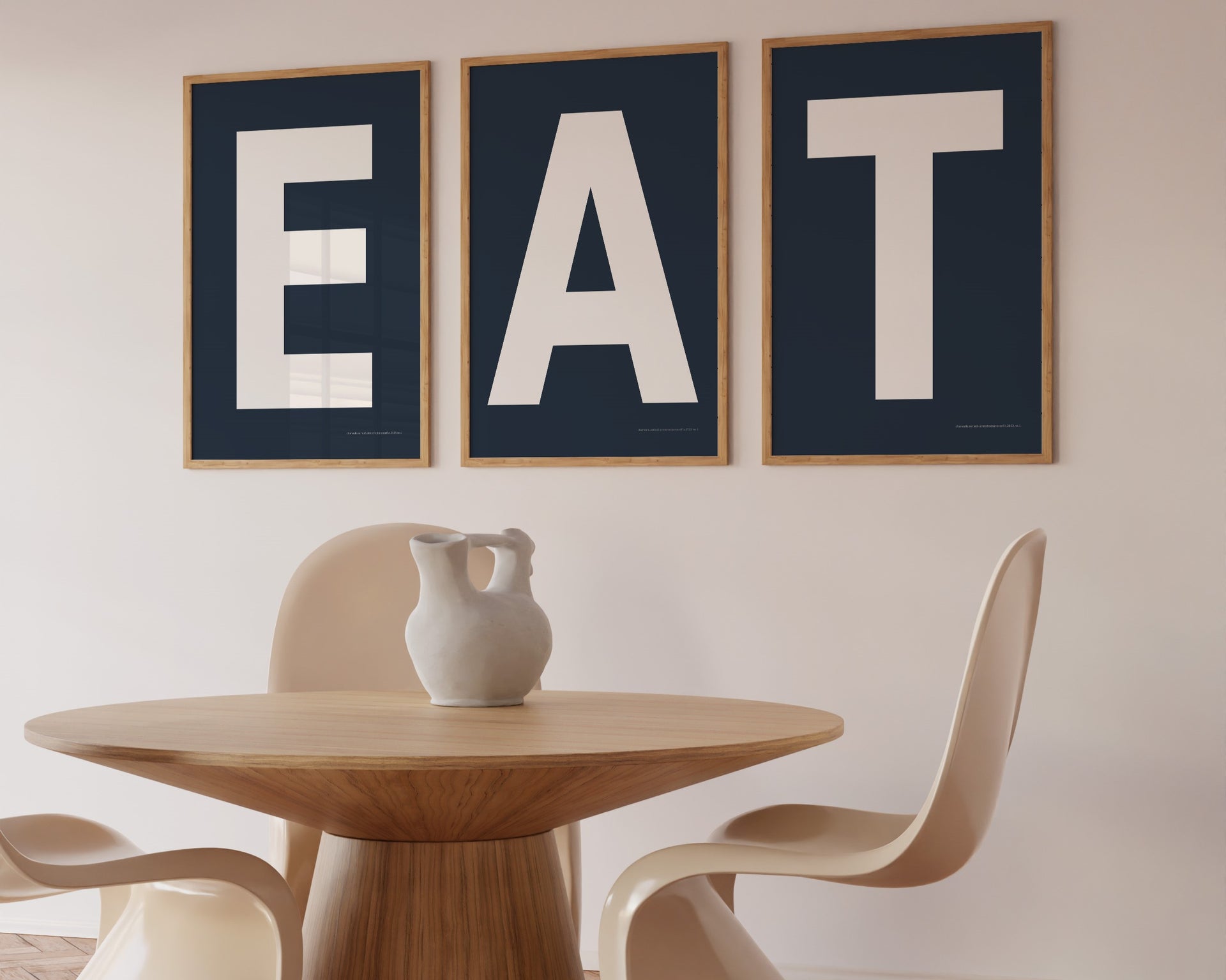 Three framed navy blue and white letter art prints spelling out the word EAT hanging in a modern dining room.