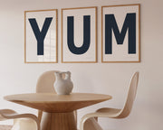 Three framed navy blue and white letter art prints spelling out the word YUM hanging in a modern dining room.