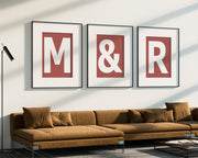 Three oversized framed Nantucket red and white letter and ampersand art prints spelling out M&R hanging above a modern sofa.