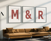 Three oversized framed Nantucket red and white letter and ampersand art prints spelling out M&R hanging above a modern sofa.