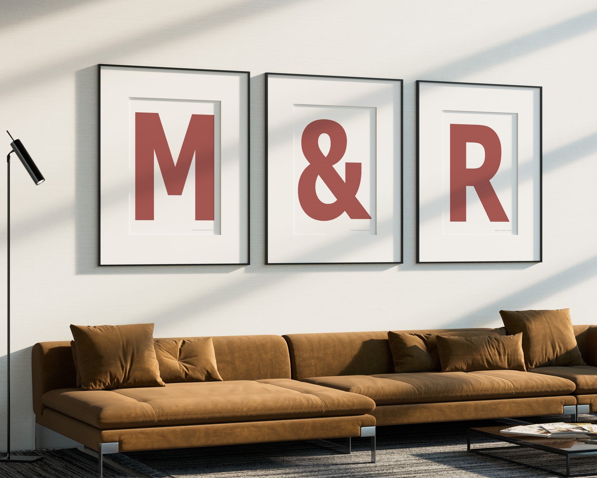 Three oversized framed Nantucket red and white letter and ampersand art prints spelling out M&R hanging above a modern sofa.