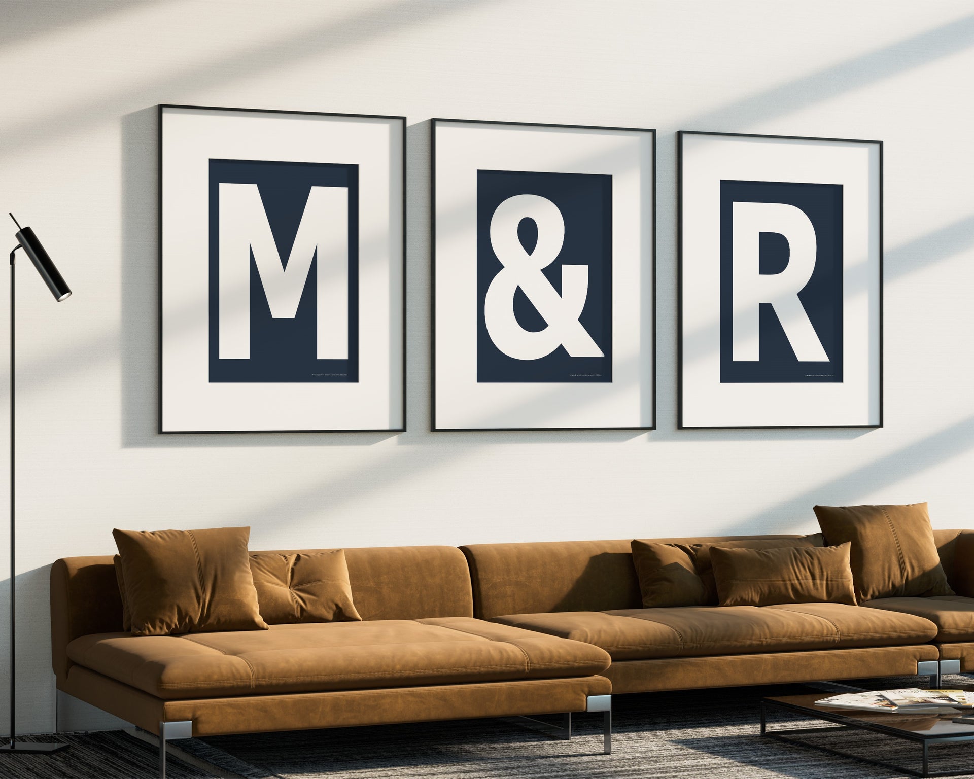 Three oversized framed navy blue and white letter and ampersand art prints spelling out M&R hanging above a modern sofa.