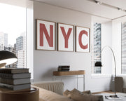 Three framed Nantucket red and white letter art prints spelling out NYC hanging on a wall in a modern living room with a view of the city.