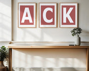 Three framed Nantucket red and white letter art prints spelling out ACK, the Nantucket airport call letters, hanging above a table in a entryway.