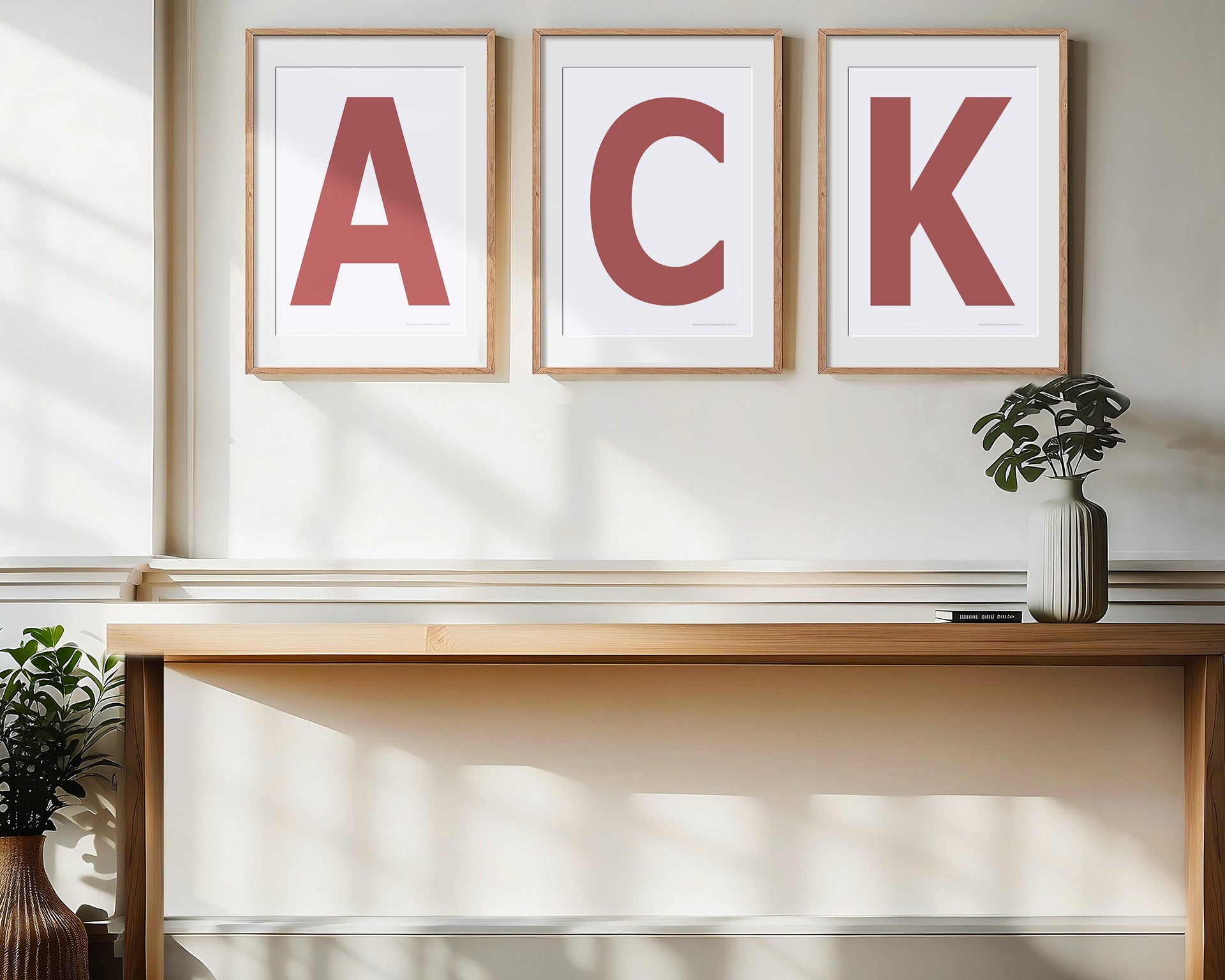 Three framed Nantucket red and white letter art prints spelling out ACK, the Nantucket airport call letters, hanging above a table in a entryway.