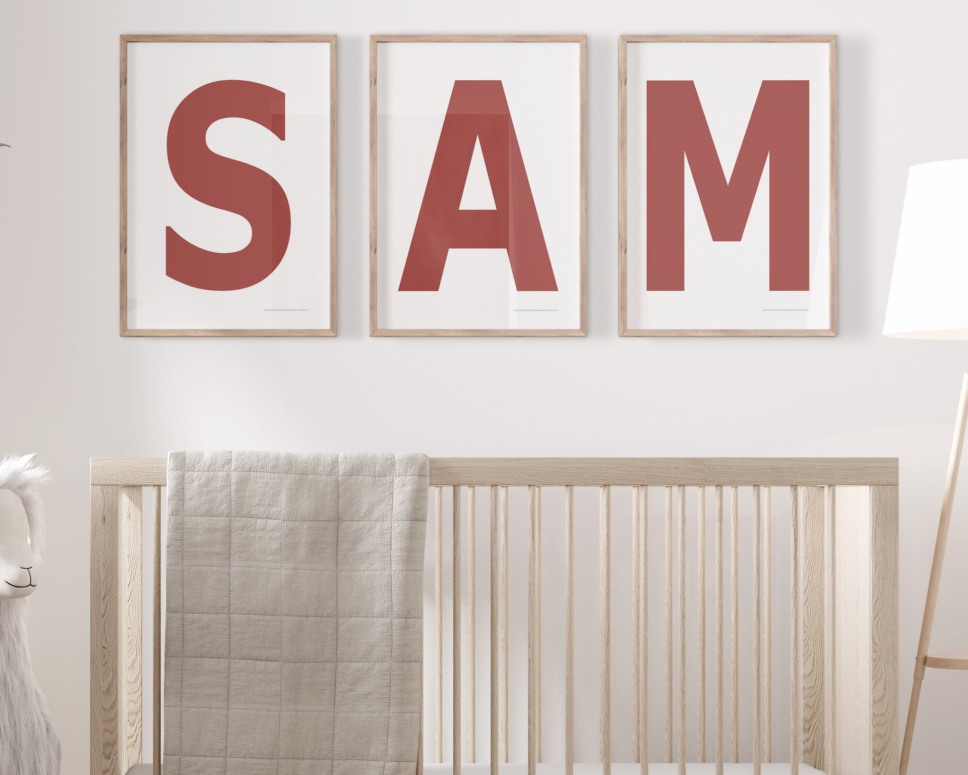 Three framed Nantucket red and white letter art prints spelling out the name SAM hanging above a crib in a neutral nursery.