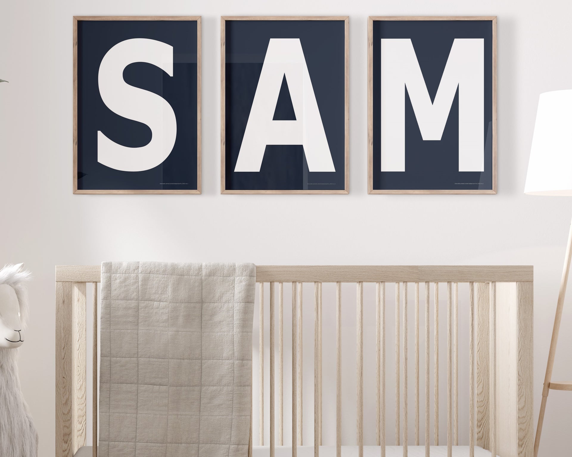 Three framed navy blue and white letter art prints spelling out the name SAM hanging above a crib in a neutral nursery.