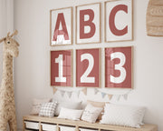 Six framed Nantucket red and white letter and number art prints spelling out ABC123 hanging on a wall in a nursery or playroom.