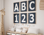 Six framed navy blue and white letter and number art prints spelling out ABC123 hanging on a wall in a nursery or playroom.