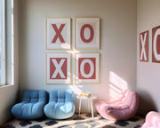 Framed letter art prints spelling out XO and XO in a modern reading nook with blue and pink chairs.