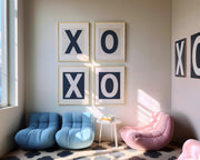 Framed letter art prints spelling out XO and XO in a modern reading nook with blue and pink chairs.