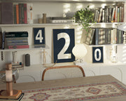Three navy blue and white framed number art prints spelling out 420 on an eclectic and modern bookshelf.