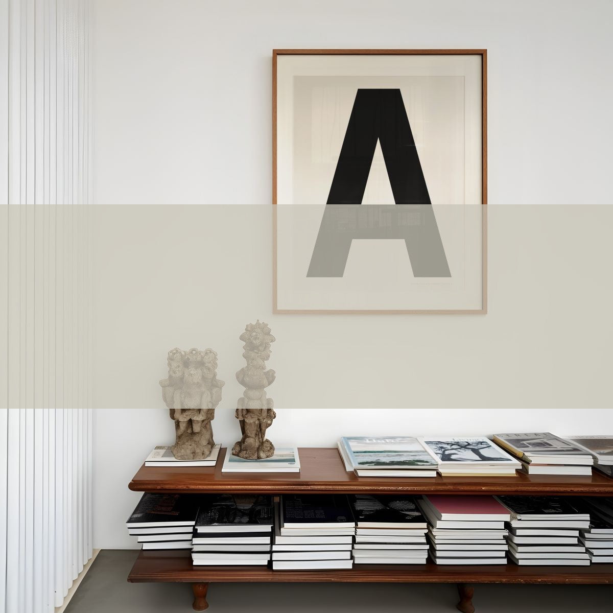 Framed white and black letter A art print hanging on a white wall above a low mid century credenza book shelf.